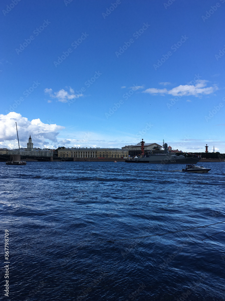 Neva water area with warships arriving to participate in the naval parade held in St. Petersburg on a blue sky with clouds.