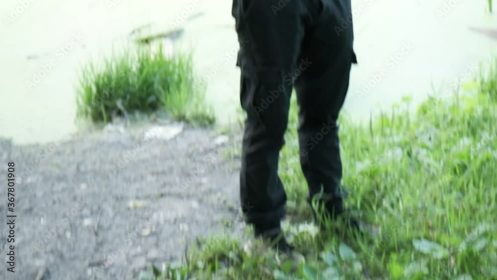 man in gas mask, black leather jacket with hood standing outdoors at forest near lake. protection from chemical weapons, virus epidemic. Post apocalyptic world. survivor, stalker after nuclear war man in gas mask, black leather jacket with hood standing outdoors at forest near lake. protection from chemical weapons, virus epidemic. Post apocalyptic world. survivor, stalker after nuclear war