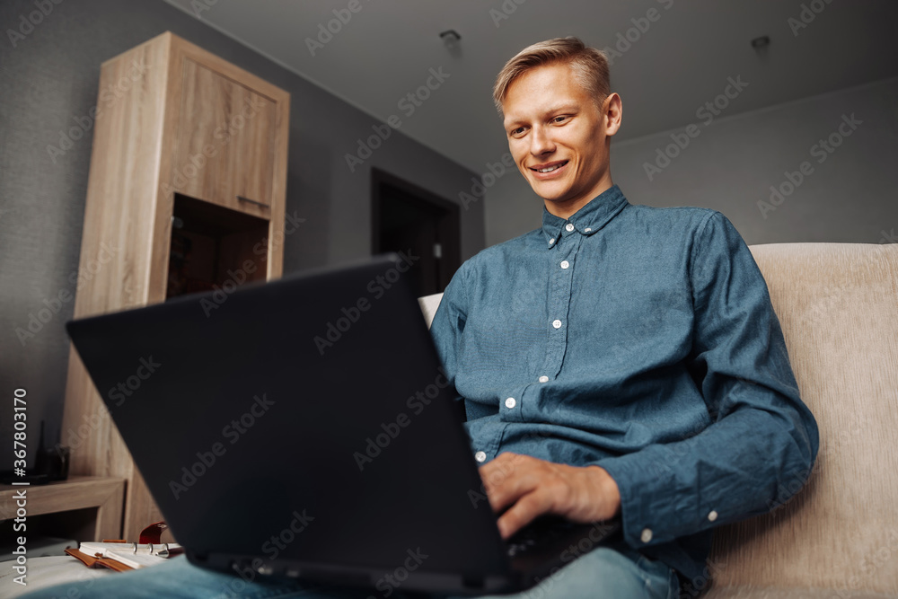 Joyful young man writes a message on a laptop while sitting on the couch at home, remote work Joyful young man writes a message on a laptop while sitting on the couch at home, remote work