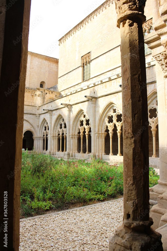 Fototapeta premium The green courtyard, column and carved stone arches of the Poblet monastery (cat. Reial Monestir de Santa Maria de Poblet).Vimbodi-and Poblet. Spain.