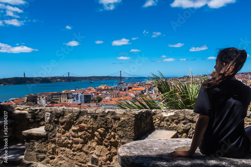 Brown-haired girl sitting alone observing the urban landscape of the city of Lisbon, Portugal.