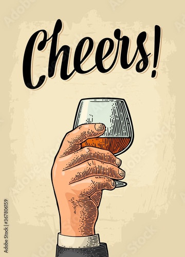 Male hand holding a glass of brandy. Cheers toast lettering.