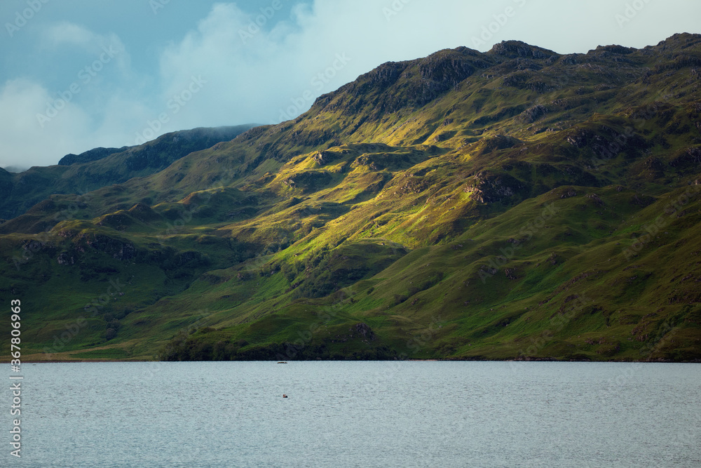 Mountain slope next to the lake illuminated by the sun in summer. Loch Morar, Highland, Scotland, UK.