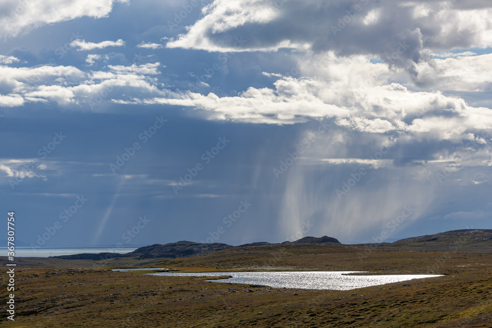 Thunderclouds lit with sunshine with the rain over Barents sea, Finnmark, Norway