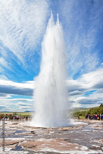 GEYSIR, ICELAND: Eruption of Strokkur geyser, observed by many tourists, on a day with remarkable cloudscape. 