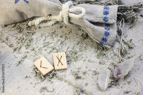 Scandinavian wooden rune Kenaz and Gebo on a rough linen cloth with amethyst crystalline, rock crystal and dried wormwood