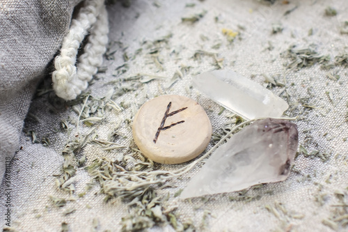 Scandinavian wooden rune Fehu, Fe, Feoh on a rough linen cloth with amethyst crystalline, rock crystal and dried wormwood photo