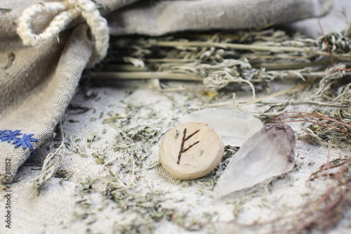 Scandinavian wooden rune Fehu, Fe, Feoh on a rough linen cloth with amethyst crystalline, rock crystal and dried wormwood photo