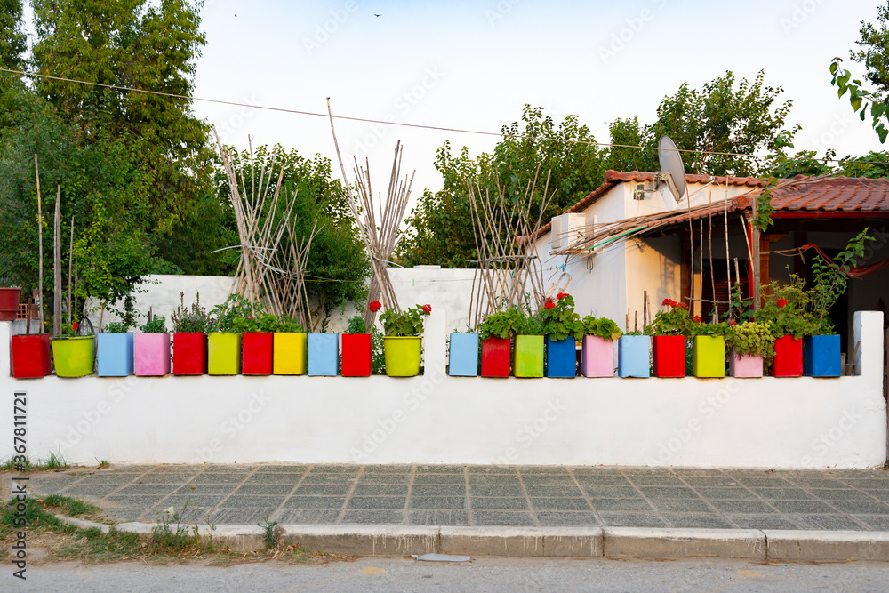 colorful plant pots with flowers on concrete white fence in the yard with garden and plants near street in Greece