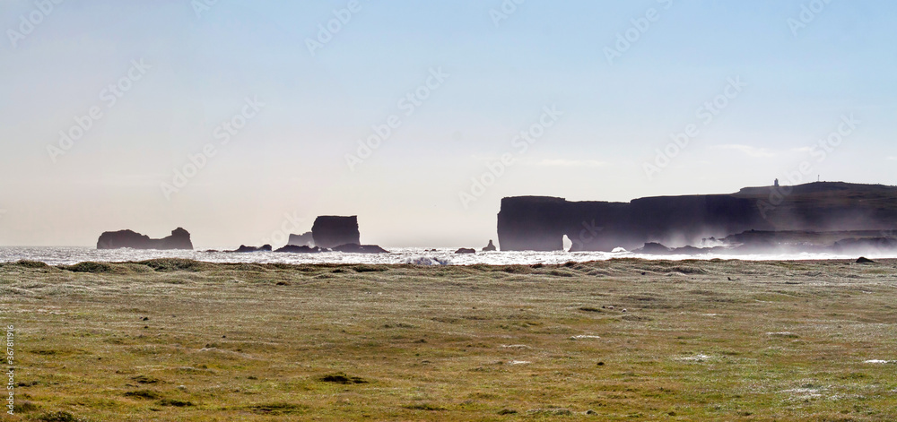Black basalt sea stacks of Reynisdrangur at Reynisfjara beach, near Vik, Southern Iceland, with strong wind.