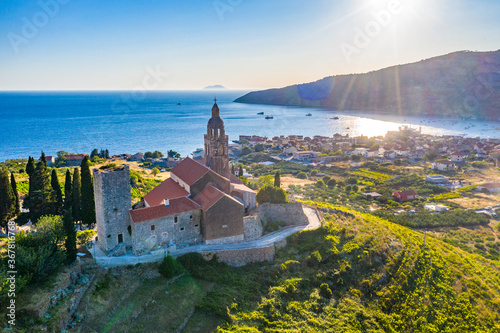 Aerial panoramic view of the cathedral St.Nicholas in Komiza city - the one of numerous port towns in Croatia, orange roofs of houses, picturisque bay, mountain is on background photo