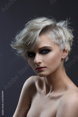Beauty portrait of a cute ash blonde girl with a short stylish haircut on a gray background.