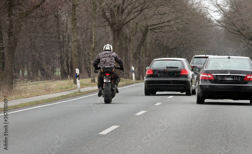 Motorradfahrer fährt schnell hinter überholenden Autos auf der Landstraße. Es ist Herbst.