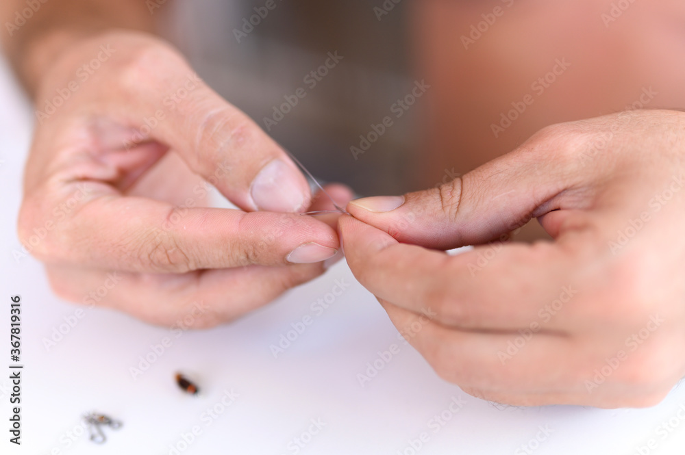men's hands tying a fishing line with a fly on a fishing hook. selective focus. step 2 men's hands tying a fishing line with a fly on a fishing hook. selective focus. step 2