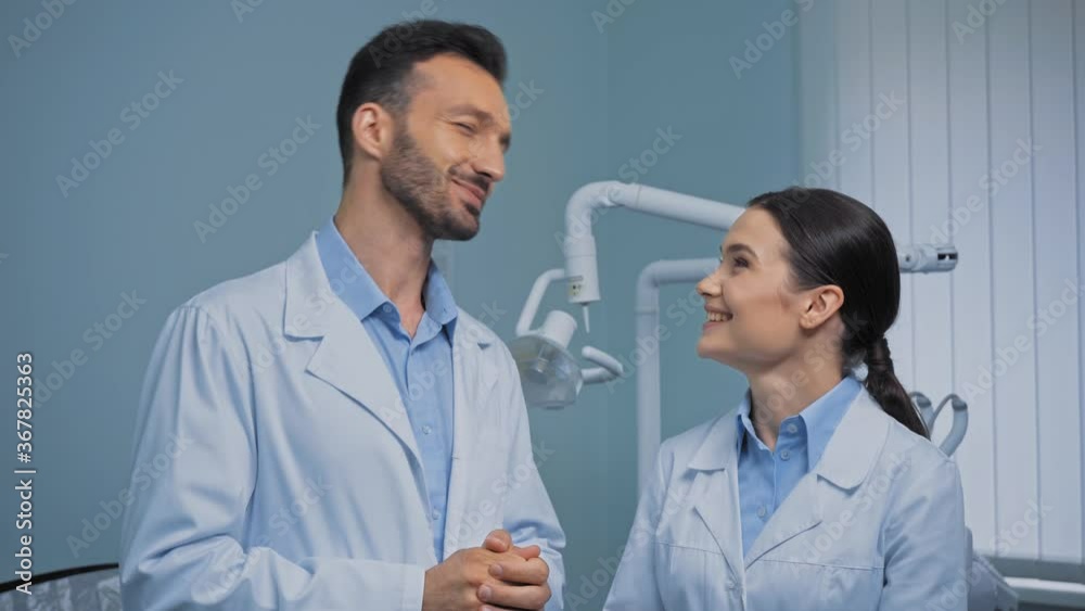 Smiling dentists in white coats talking in clinic Smiling dentists in white coats talking in clinic