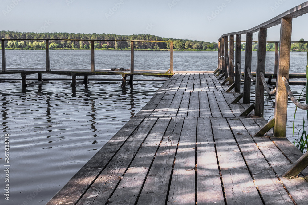 Wooden pier on the lake. Rural landscape. Place of power. The beauty of the countryside. Pacification of nature. An ideal place for meditation. Boardwalk pier for fishing.