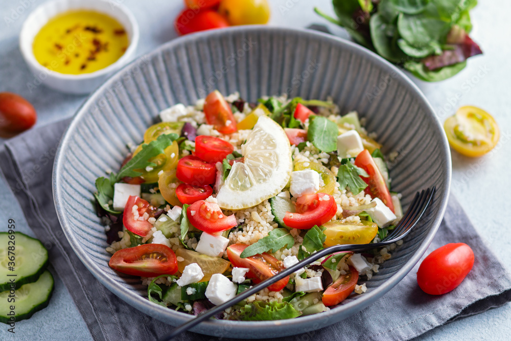 Salad with bulgur, cherry tomatoes, feta cheese and green herbs on concrete table top. Middle Eastern tabbouleh salad, top view