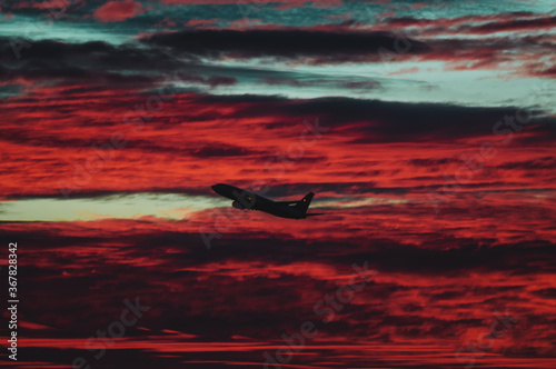 Passenger jet airplane trimmed against the clouds taking off during very red sunrise from spanish airport in a cloudy day