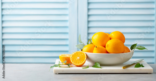 Fresh Meyer lemons in white bowl on marble board. Blue background. Copy space.