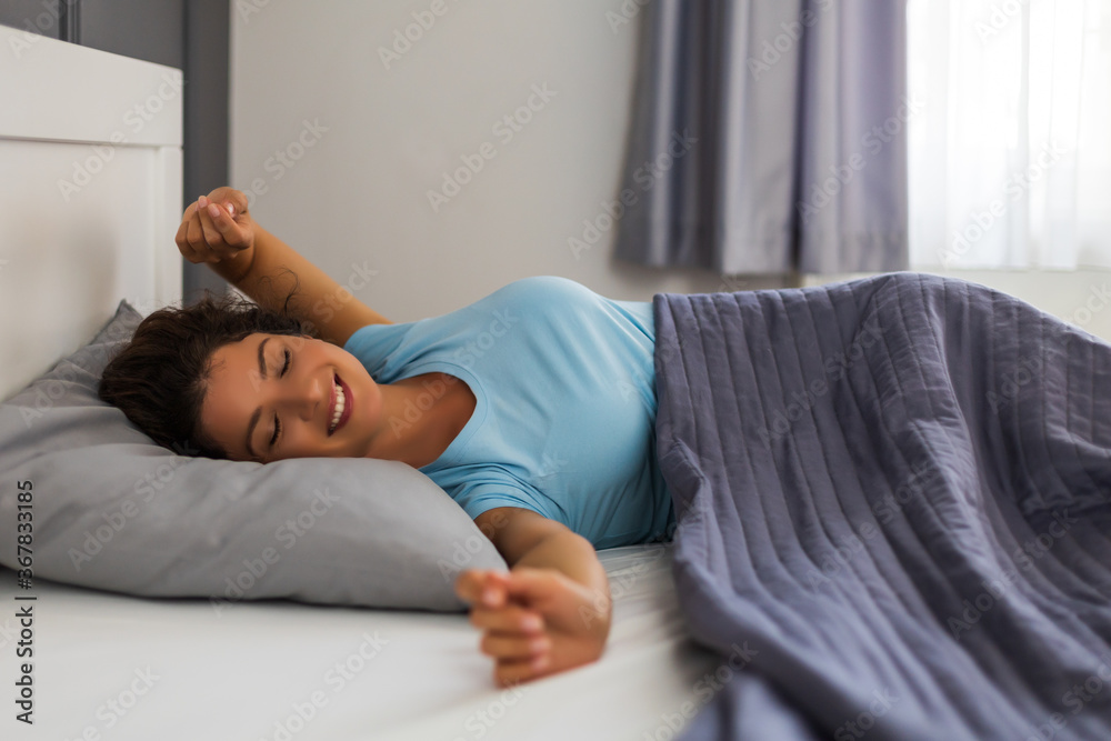 Beautiful woman waking up and stretching with a smile in the bedroom.	