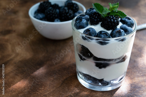 Cottage cheese dessert with blueberries, blackberries and mint in a transparent glass glass. On a wooden background. Yummy.