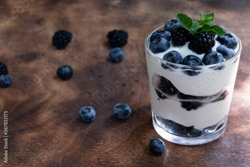 Cottage cheese dessert with blueberries, blackberries and mint in a transparent glass glass. On a wooden background. Yummy.