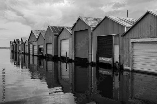 Black and white photo of boat houses on pier with reflection © Brian