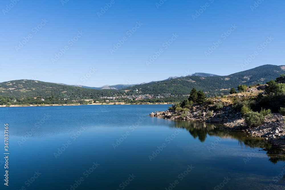 The shore of a water reservoir surrounded by green mountains in Navacerrada The shore of a water reservoir surrounded by green mountains in Navacerrada
