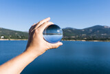 Hand holding a crystal ball reflecting the landscape of a lake of a water reservoir