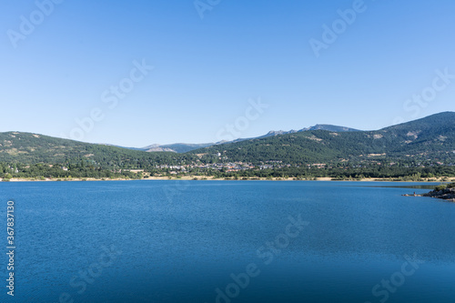 Calm water from a reservoir surrounded by green mountains in Navacerrada