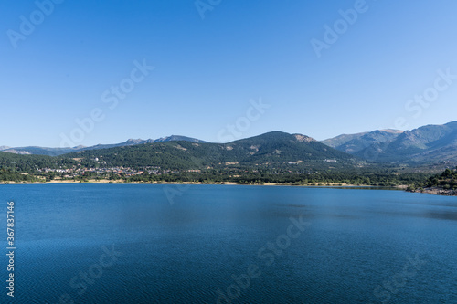 Panoramic view of a water reservoir surrounded by green mountains in Navacerrada