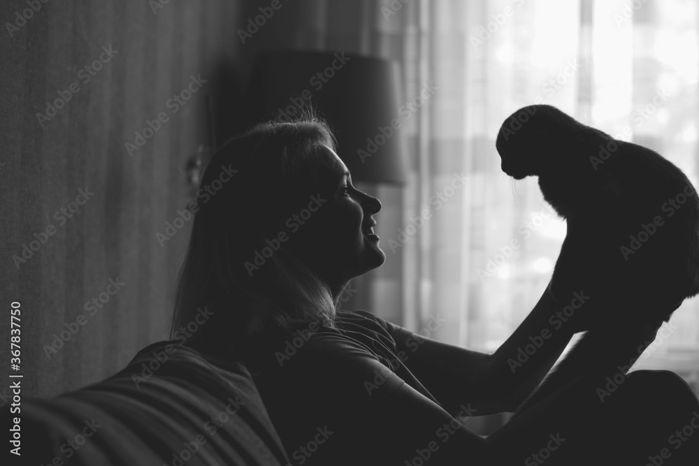 A woman at home sits on the sofa and holds a fold cat in her hands black and white silhouette photo