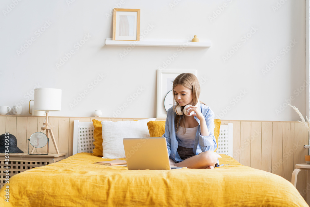 Pretty young student working at home on her laptop computer sitting on her bed Pretty young student working at home on her laptop computer sitting on her bed