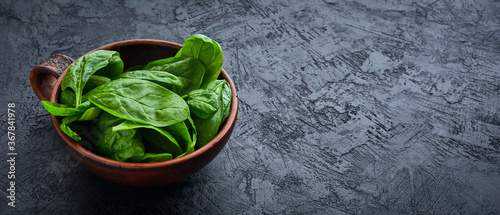 Spinach in the bowl on the dark background. Washed fresh mini spinach, green grass, vitamins salad.