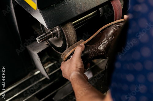 Male shoemaker repairing shoe heel on grinding machine. Cobbler at work.