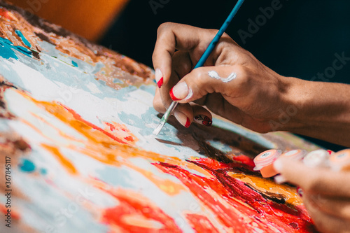 Brush in the hand of an artist drawing a picture on the canvas
