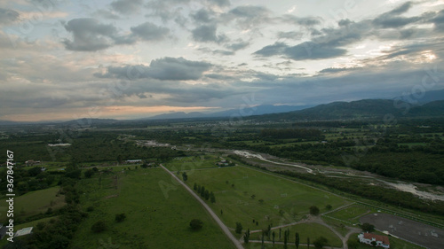 Rural landscape. Aerial view of the countryside. The river flowing across the plantation fields, forest and mountains at sunset.