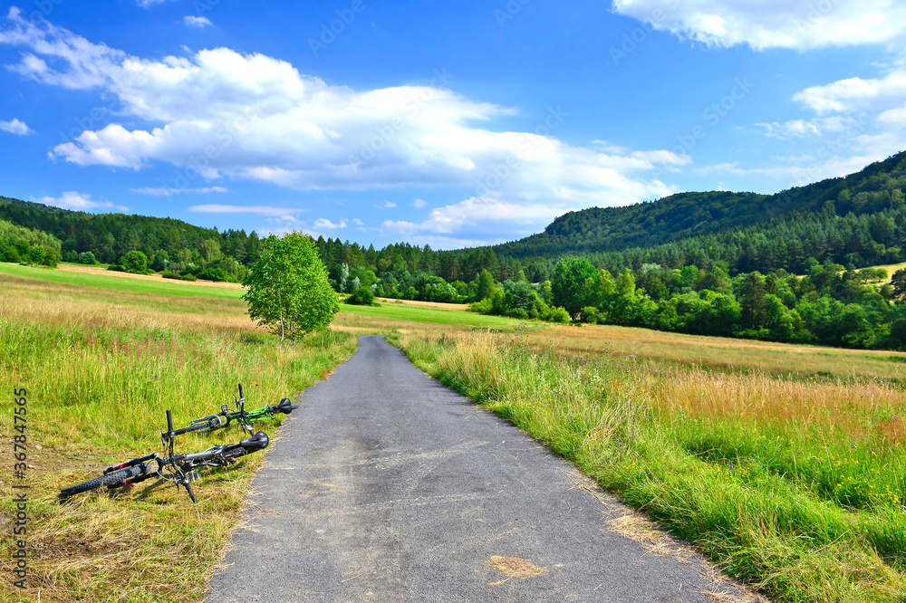 Fototapeta premium Mountain biking in summer sunny day. Two bikes are lying on the ground, next to a asphalt dirt road. 