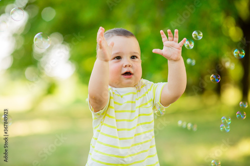 Happy baby boy one year plays with soap bubbles summer outdoors. Children's Lystyle