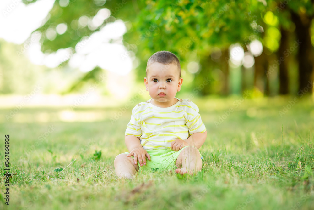 Happy baby boy sits on the green grass in the summer in the park. Children's Lifestyle Happy baby boy sits on the green grass in the summer in the park. Children's Lifestyle