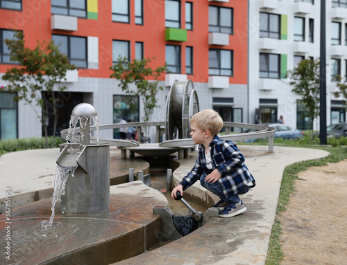 A little boy with blond hair plays with water in a modern playground. Drops of water fly around.