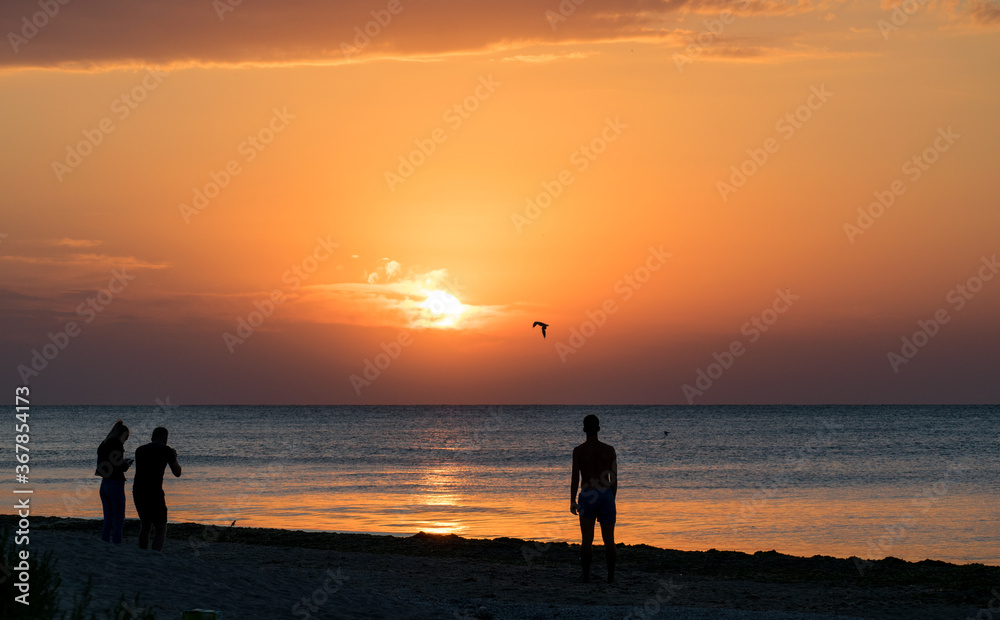 People on the beach at sunrise. Silhouettes. Admire the sunrise at sea