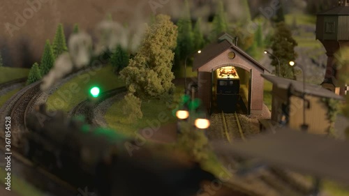Model train station at miniature forest. Model railroad in forest and moving vintage steam locomotive.