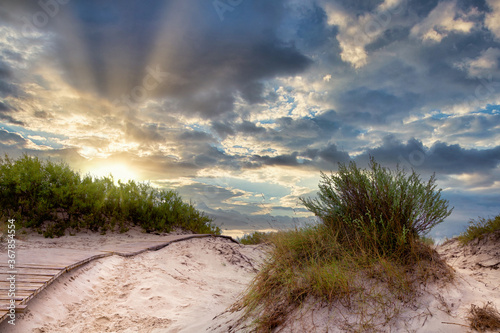 Wooden path through sand dunes on the Baltic sea in Ventspils against the backdrop of a dramatic sunrise or sunset © olmax1975