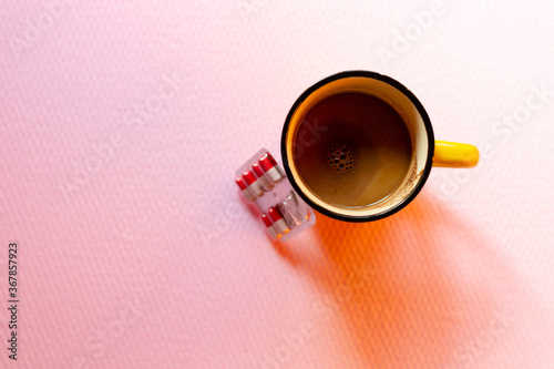 Top view on red-white pills in blister pack and cup of black coffee on pink color background