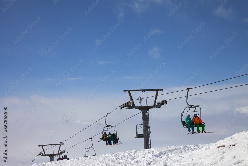 Skiers and snowboarders go up on chair-lift, snowy off-piste ski slope and high mountains
