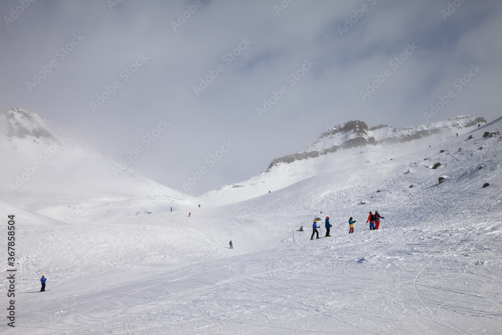 Skiers and snowboarders descent on snowy ski slope and overcast misty sky
