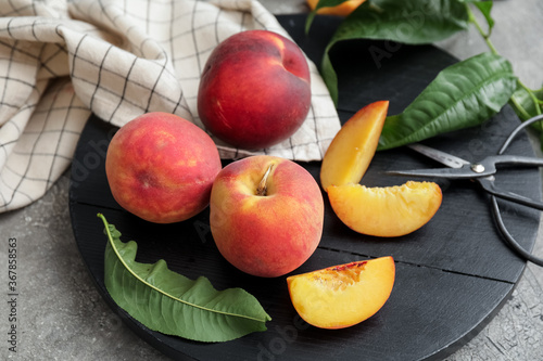 Board with ripe peaches on grey background