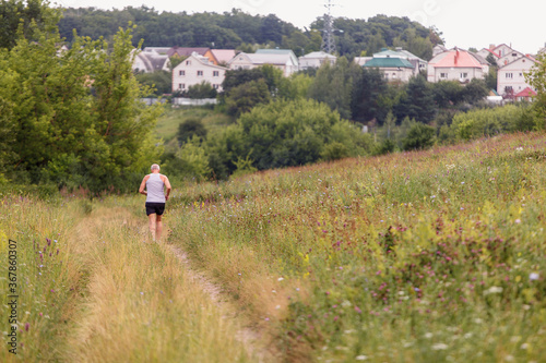 Old man runs along a flowering field outside the city
