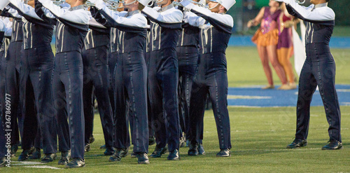 Marching band on a field playing for a crowd. . Marching in a line with trumpets and other instruments playing music.